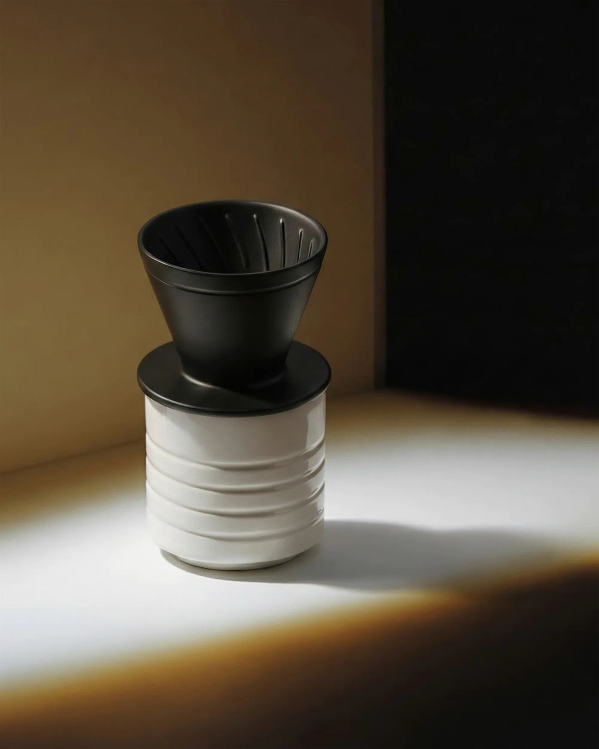 Black ceramic coffee dripper on a ringed white porcelain cup in a band of warm low light