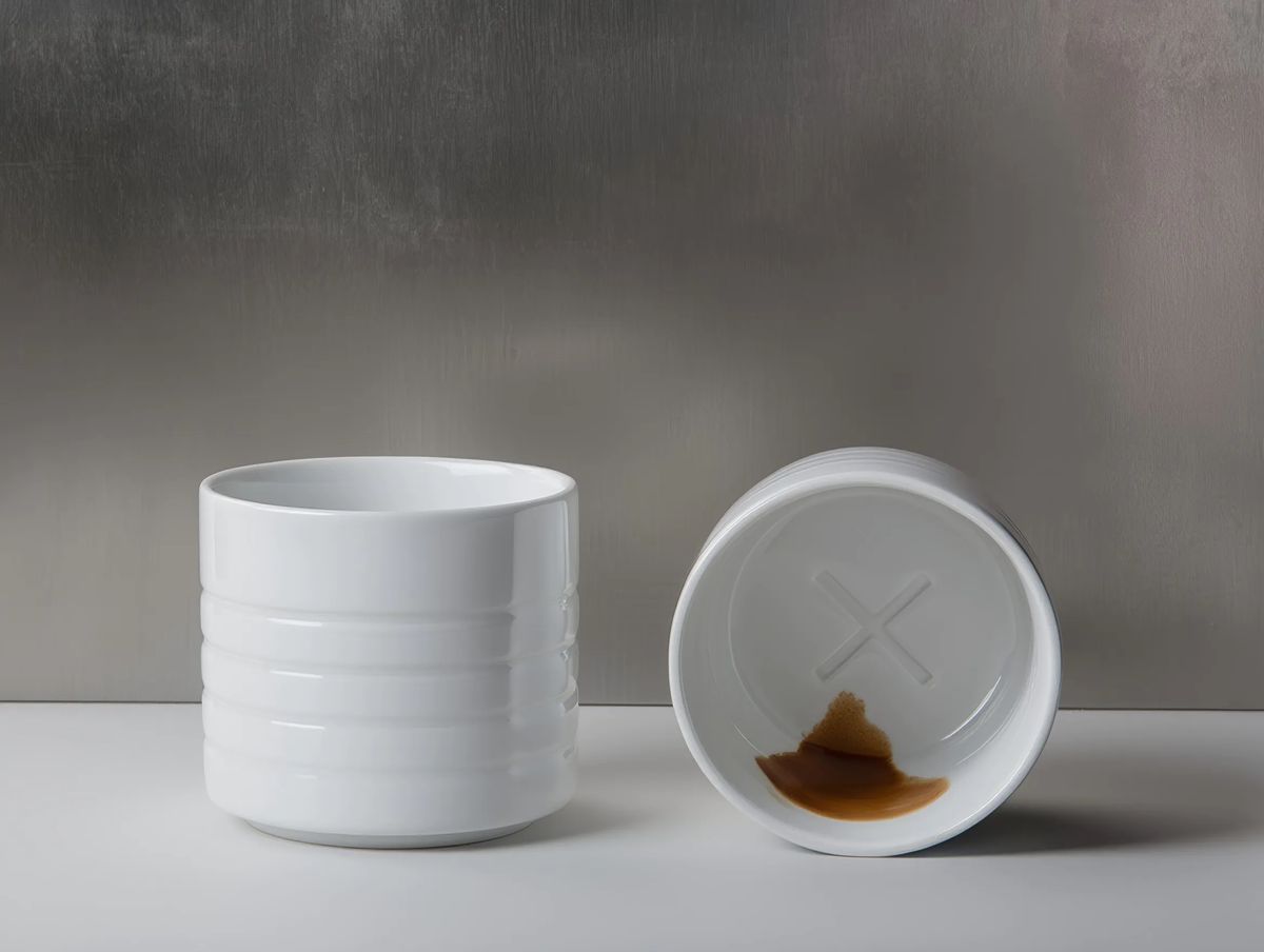 Two white porcelain cups, one tipped over to show a relief cross on the base stained with coffee