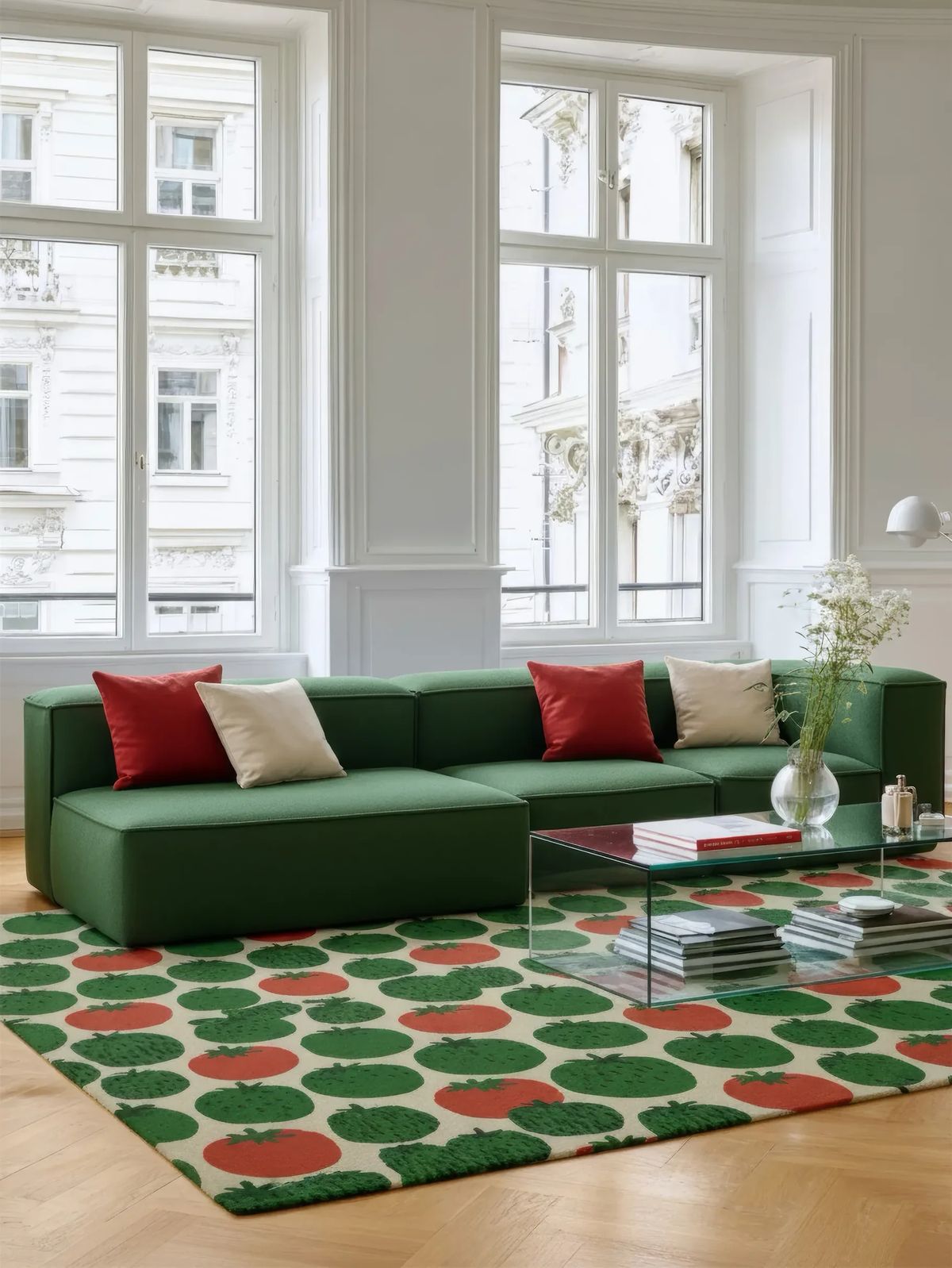 Strawberry-patterned rug in green and red under a green modular sofa and glass table in a bright room