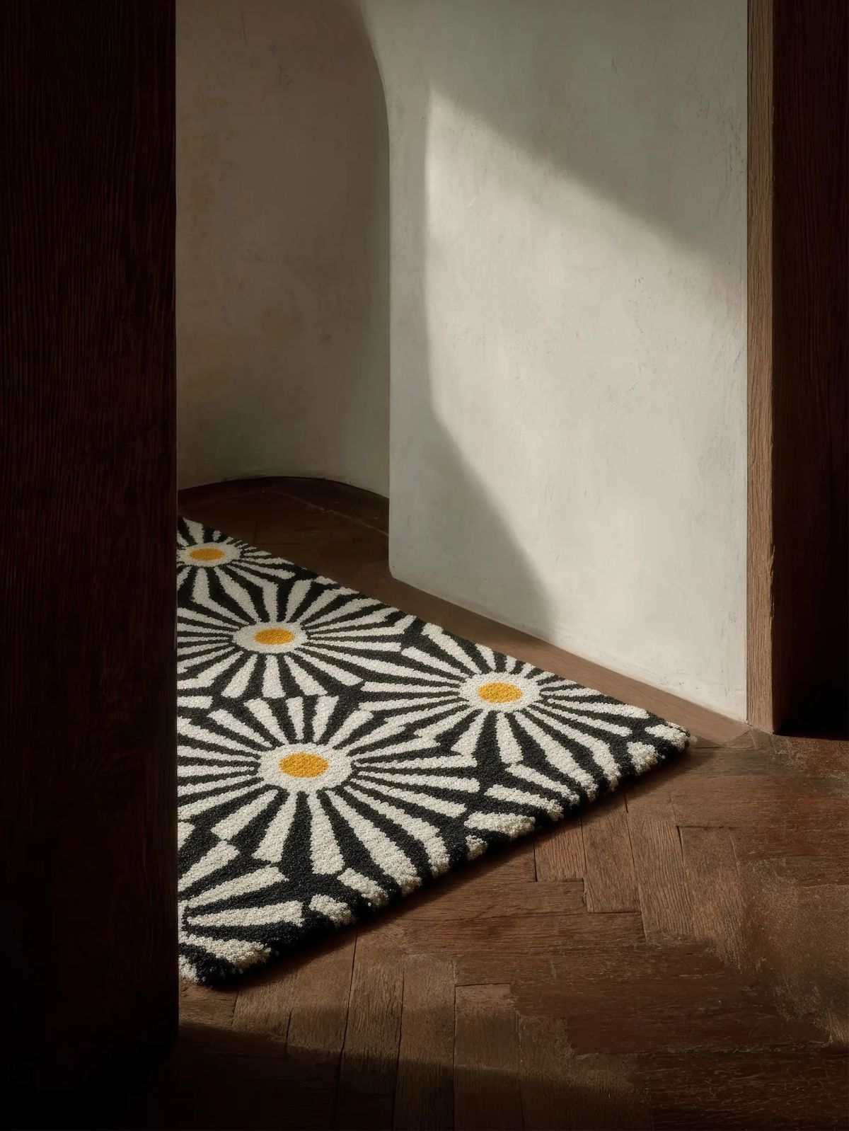 Tufted black and white rug with radiating daisy motifs and yellow centres in a sunlit doorway