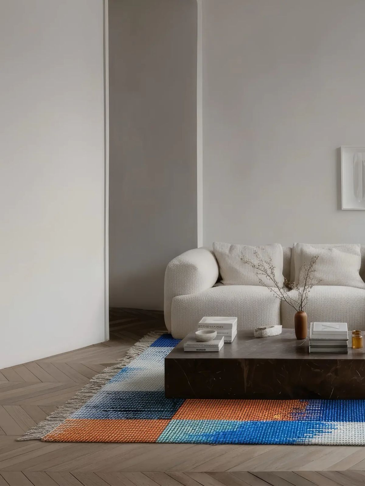 Fringed rug in blue, orange and white blocks under a dark stone coffee table and cream sofa