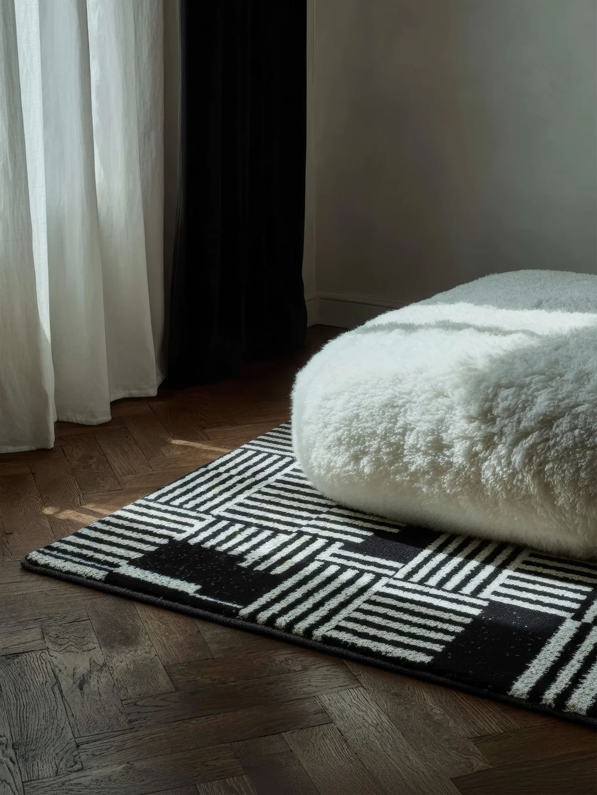 Black and white striped patchwork rug under a fluffy white sheepskin pouf on dark parquet
