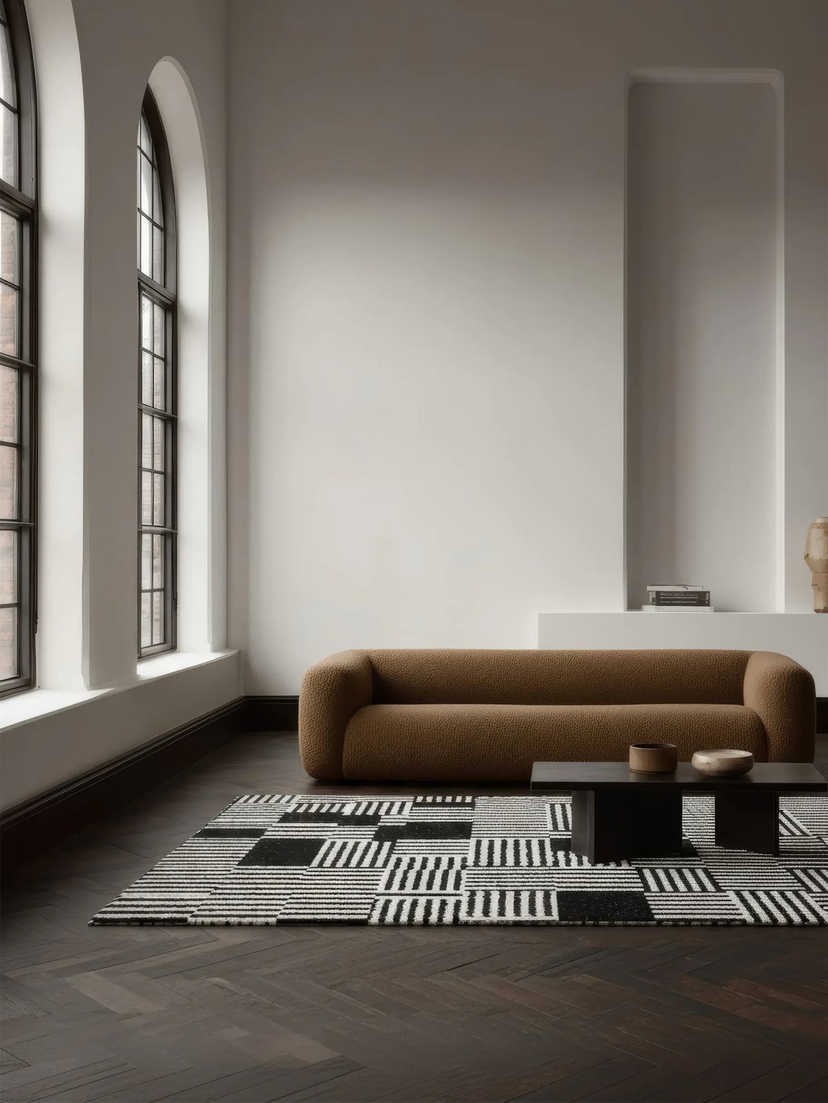 Black and white striped block rug before a camel bouclé sofa in a tall room with arched windows