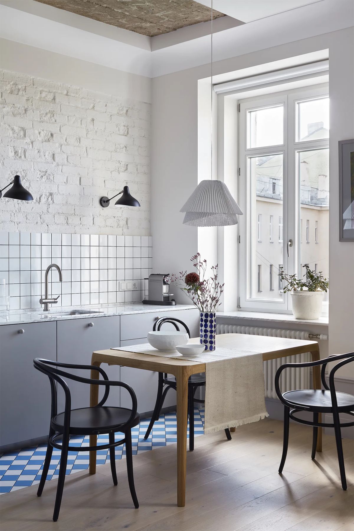 Kitchen with white brick wall, grey cabinets and bentwood chairs around an oak table by a tall window