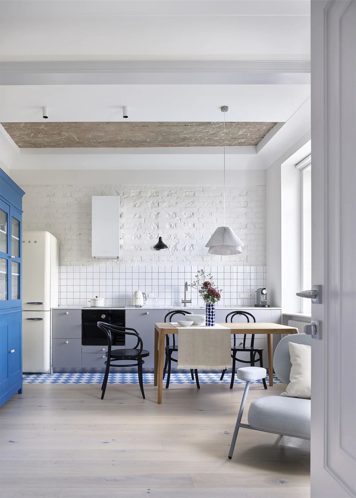 Open kitchen with blue glazed cabinet, cream fridge, white brick wall and blue-and-white tiled floor