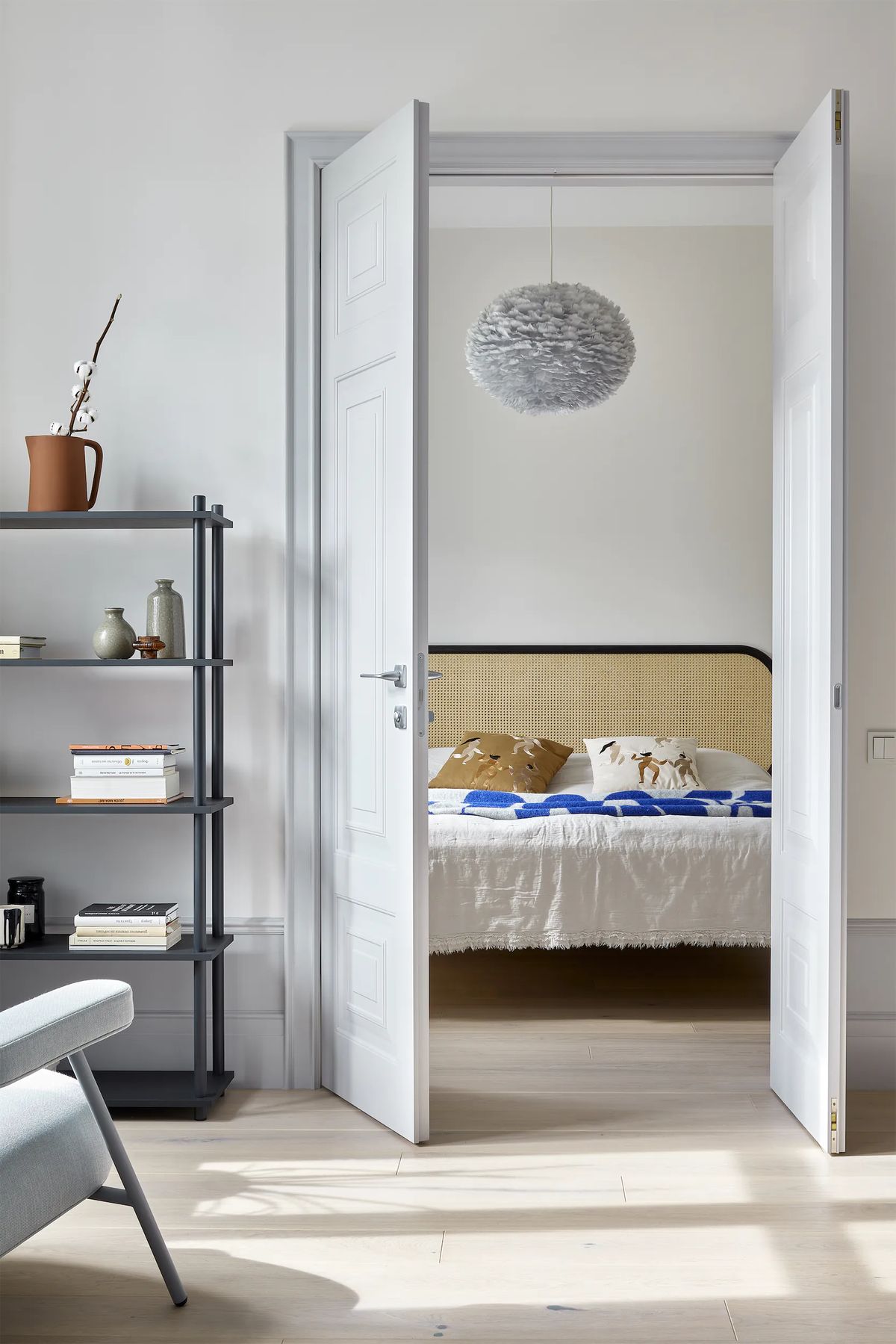 Double doors open from the living room onto a bedroom with a cane headboard and feather pendant