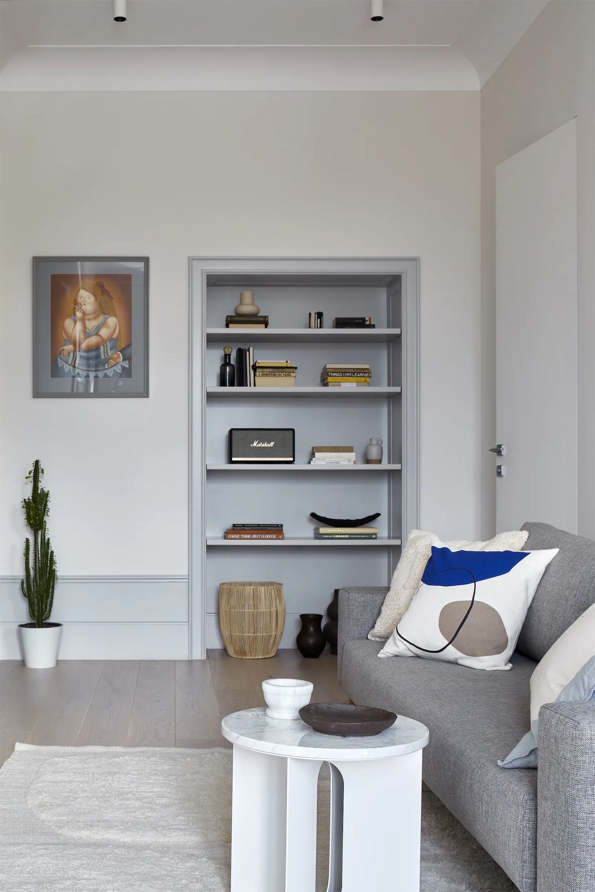 Living room with grey sofa, marble side table, framed painting and grey shelving set into a wall niche