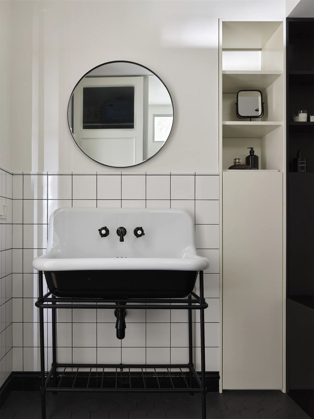 Bathroom with white enamel basin on a black steel stand, round mirror and white grid tiles