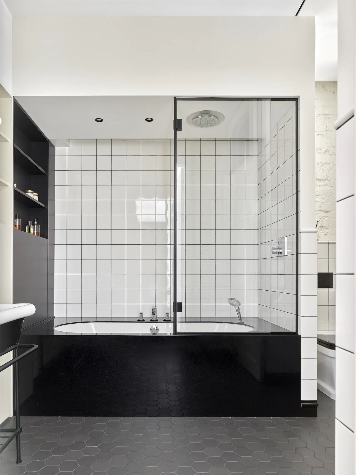 Bathtub in a black-tiled base with glass screen, white wall tiles and dark hexagonal floor