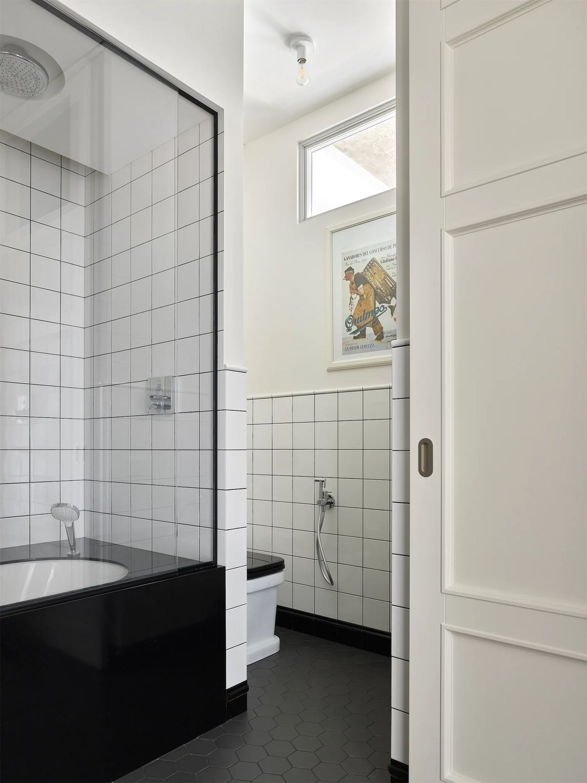 Bathroom with glazed bath screen and a separate WC with a high window seen past a panelled door
