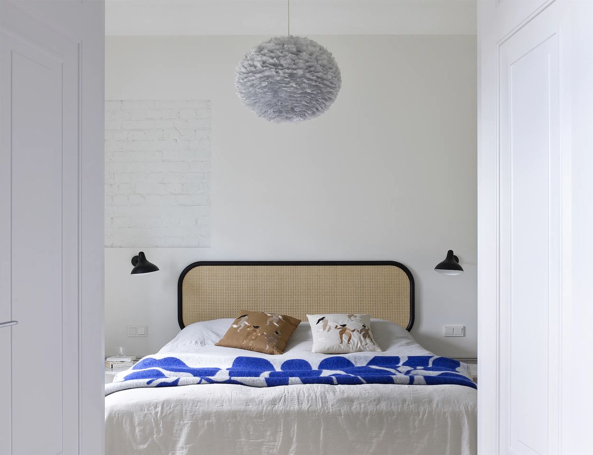 Bedroom of the Chistye Prudy apartment with cane headboard, blue throw and grey feather pendant