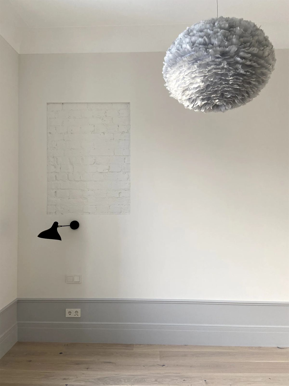 Empty bedroom wall with a whitewashed brick panel, black wall lamp and grey feather pendant