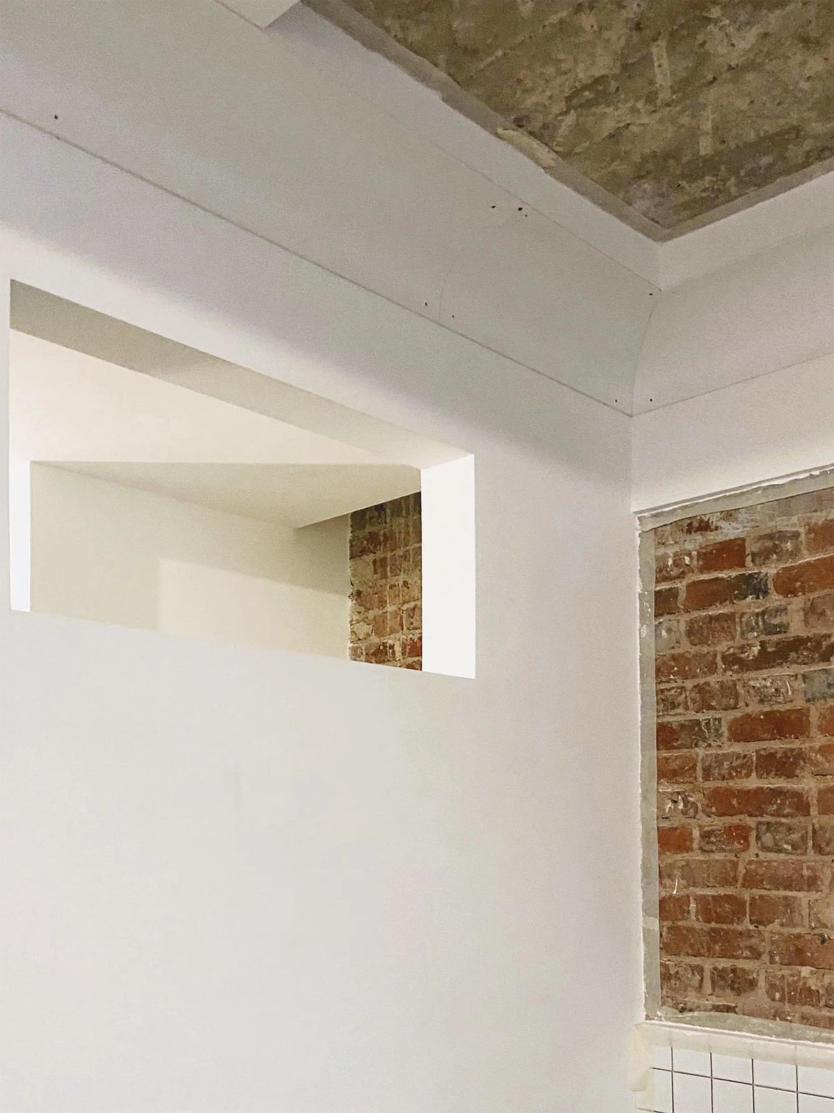 Plastered walls with an interior opening and a framed panel of exposed red brick under the old ceiling