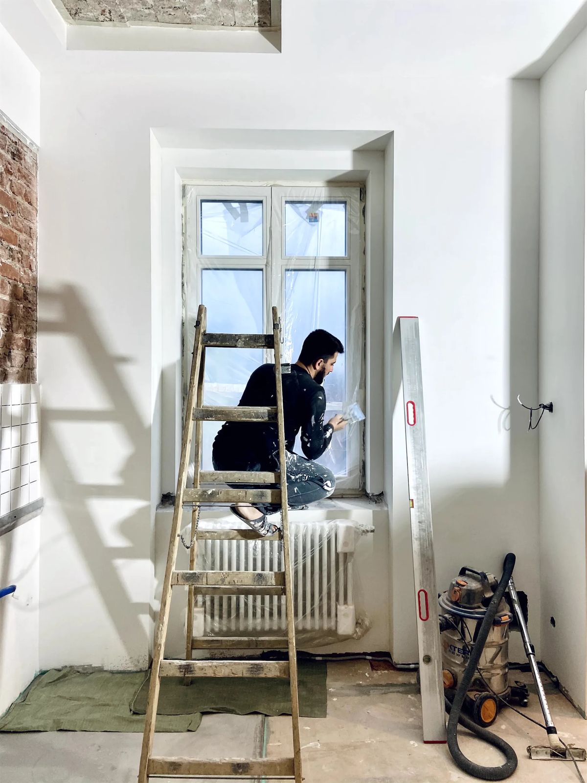 Builder sealing a window on a stepladder in a freshly plastered room during renovation