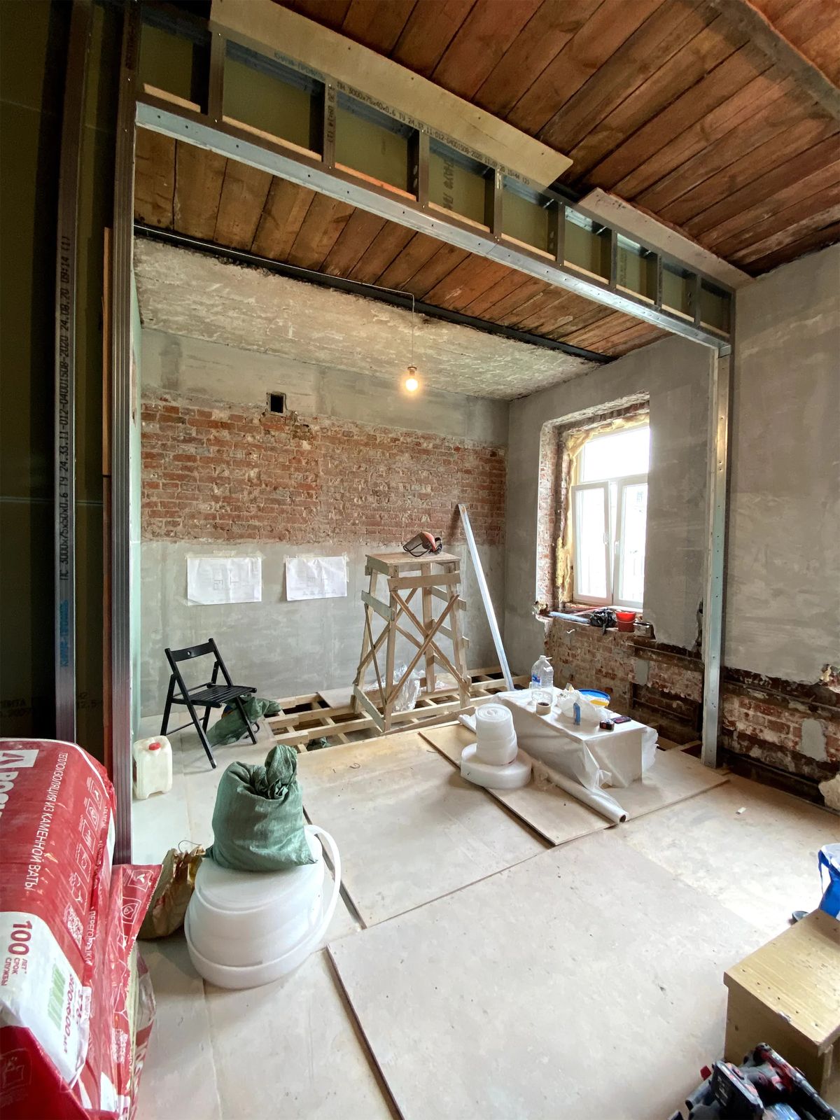 Renovation site with steel stud framing under an old timber plank ceiling and exposed brick