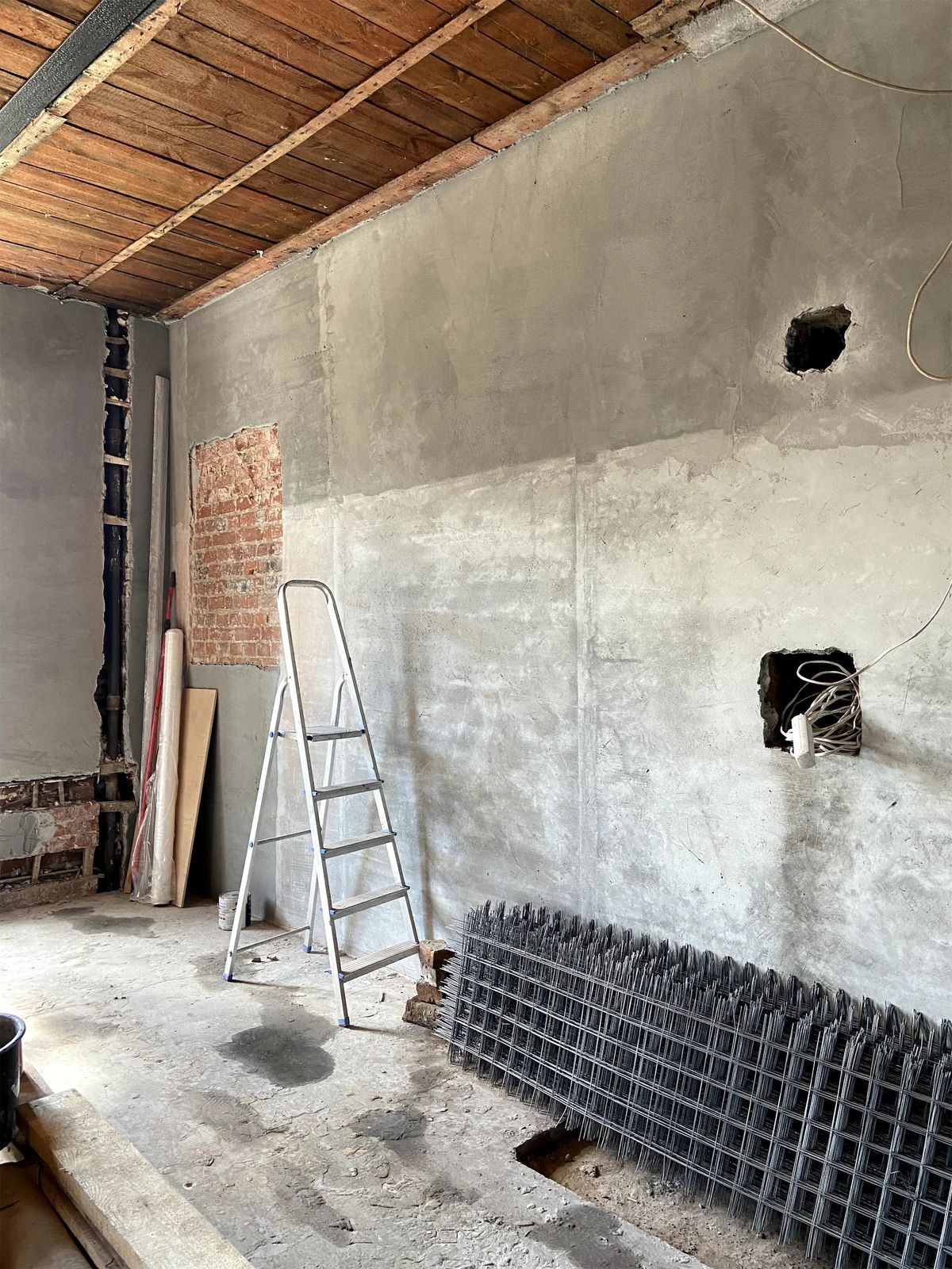 Stripped room with concrete-rendered walls, timber ceiling, aluminium stepladder and rebar mesh