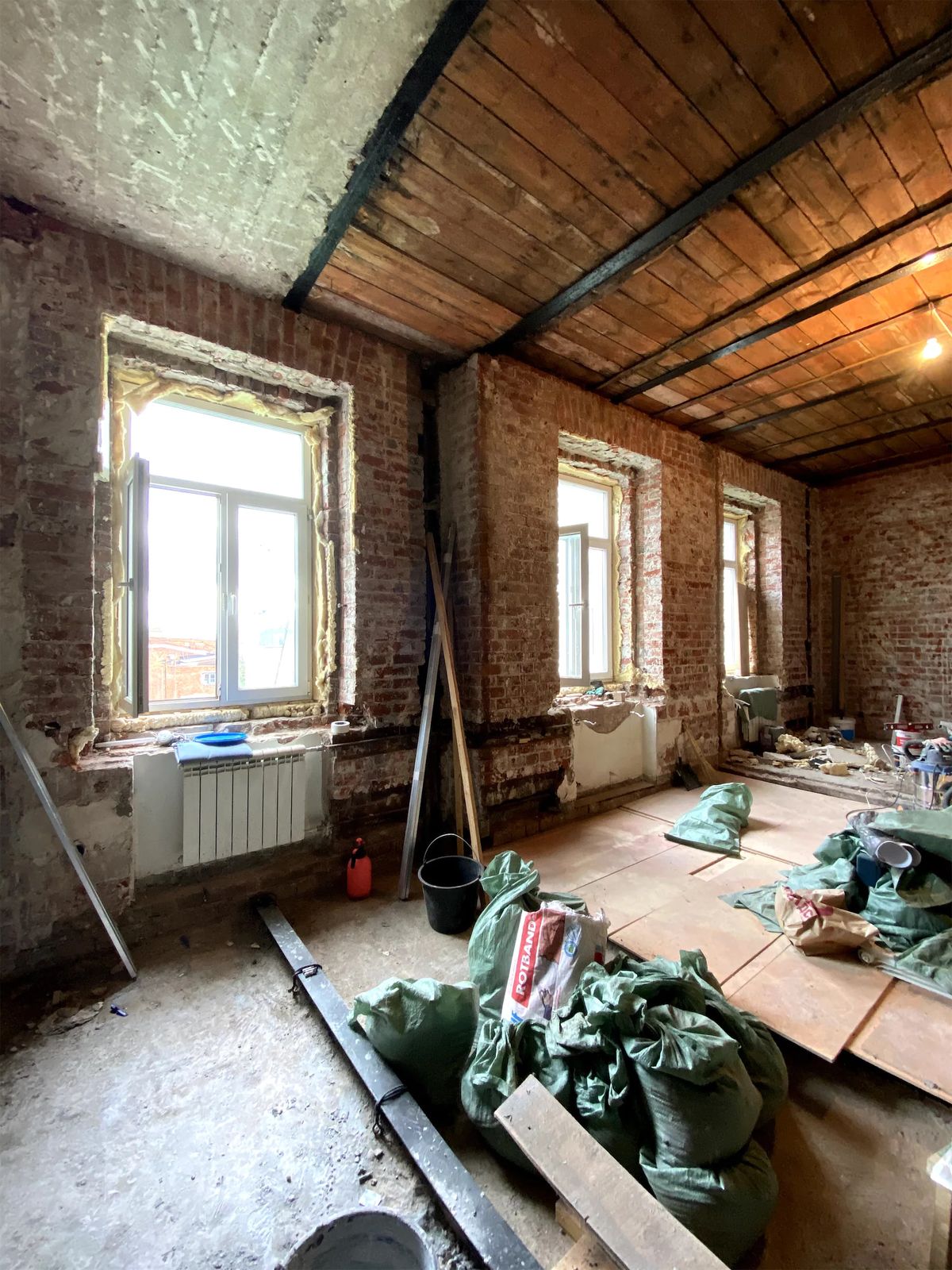 Gutted apartment with bare brick walls, new windows, timber plank ceiling and rubble sacks