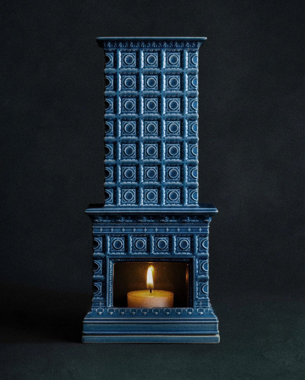 Miniature blue glazed tiled stove with a tealight glowing in its firebox