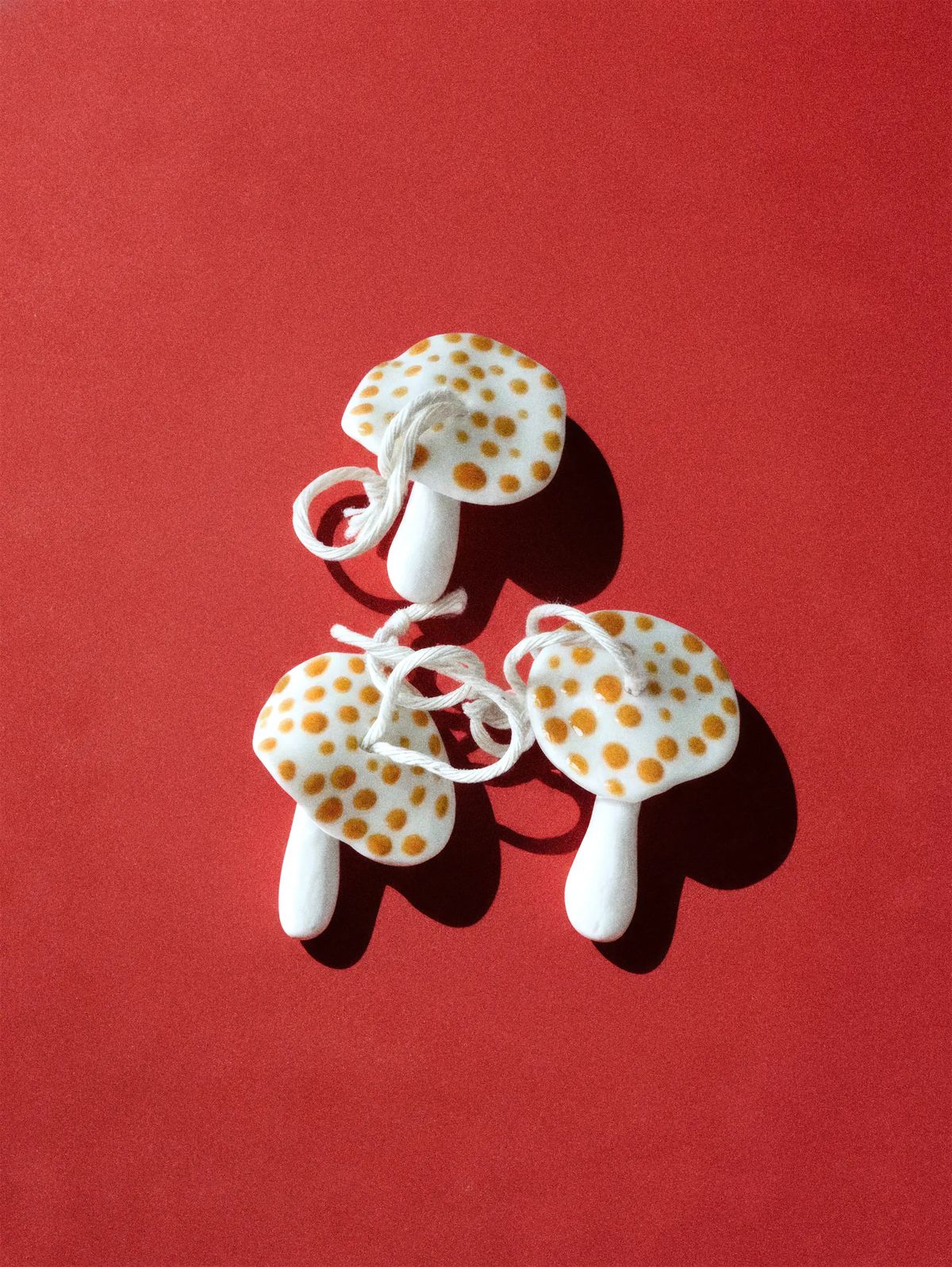 Three white porcelain mushroom ornaments with orange spots and cotton string loops on red paper