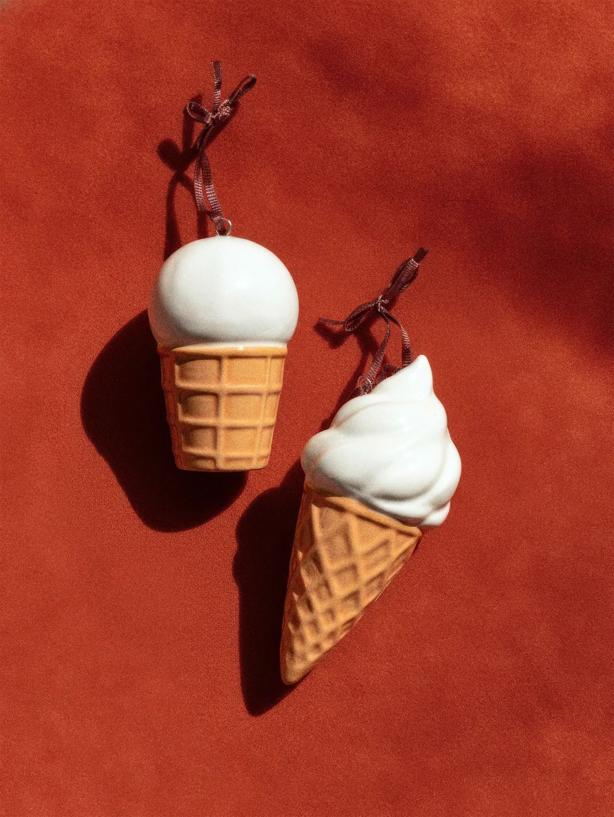 Two ceramic ice cream cone ornaments, a scoop and a soft serve, hung on brown ribbons on terracotta
