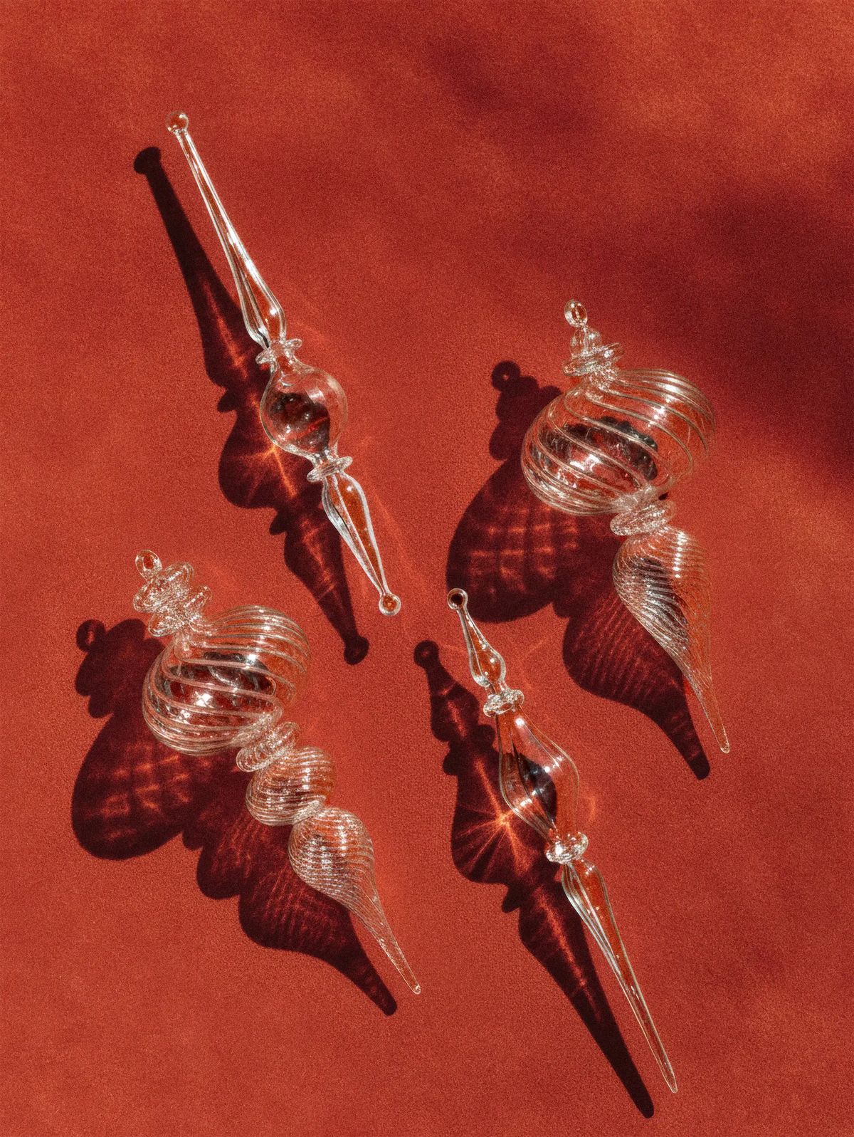 Four clear blown-glass spiral icicle ornaments casting patterned shadows on rust-red suede