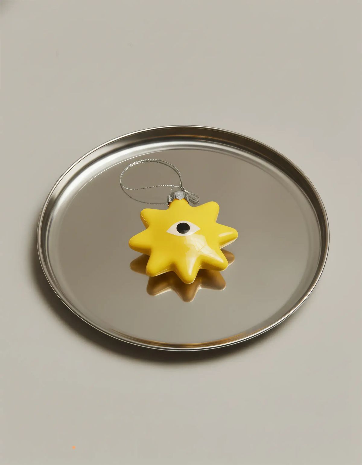 Glossy yellow star ornament with a single painted eye lying on a polished steel tray