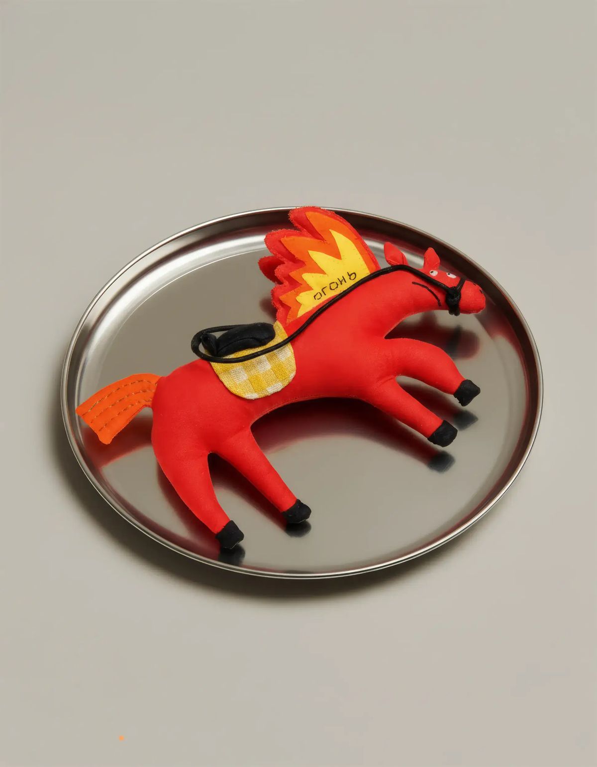 Red stuffed fabric horse with an orange flame mane and embroidered lettering on a steel tray