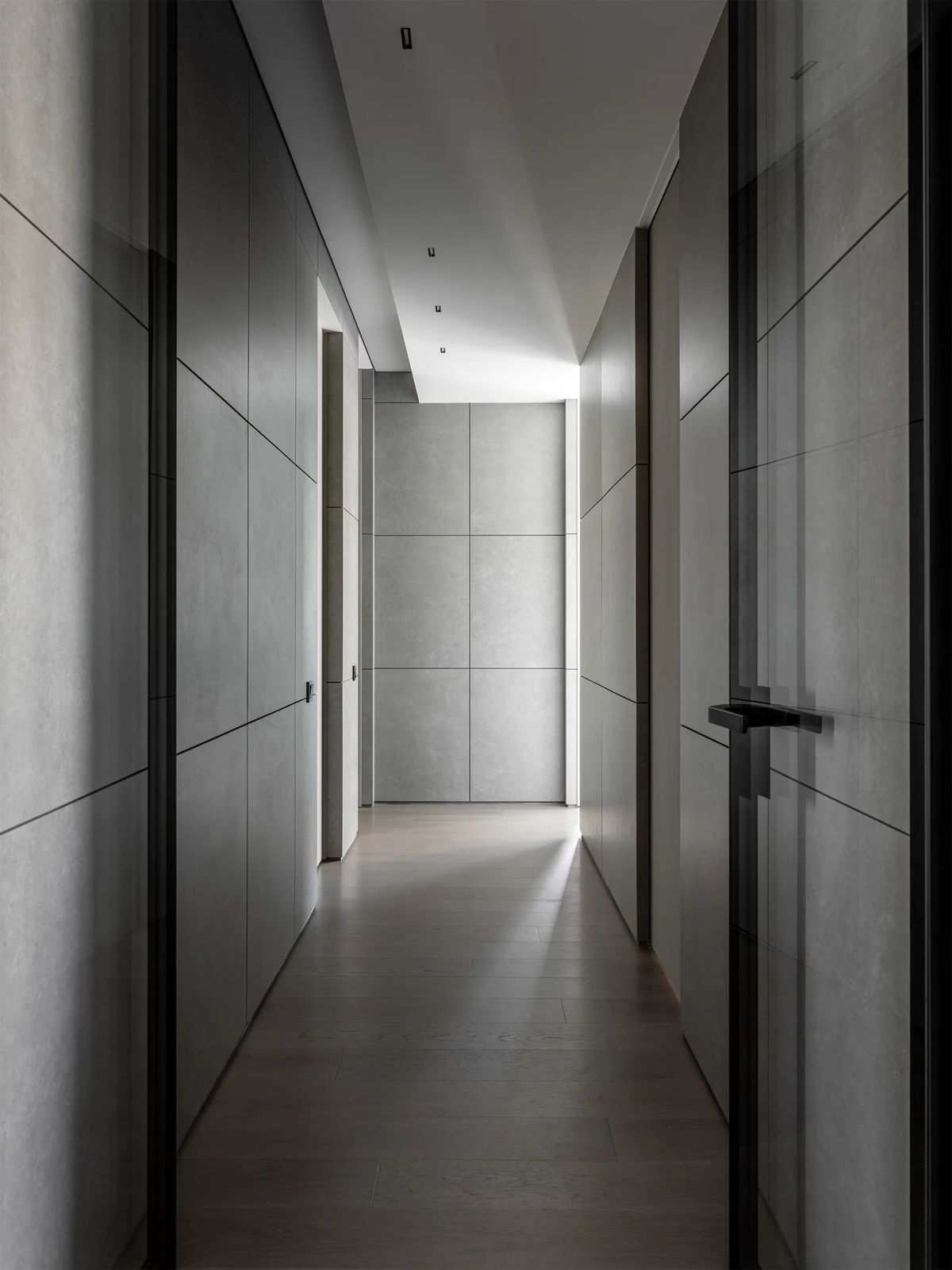 Long corridor lined with grey stone-effect wall panels, hidden doors and an oak floor lit from the end