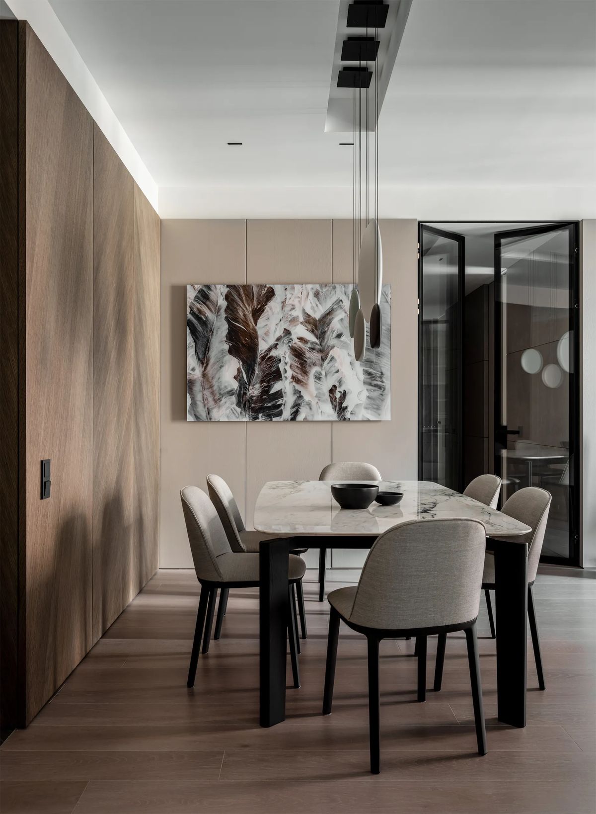 Dining area with a marble table, upholstered grey chairs, walnut wall panels and a feather painting