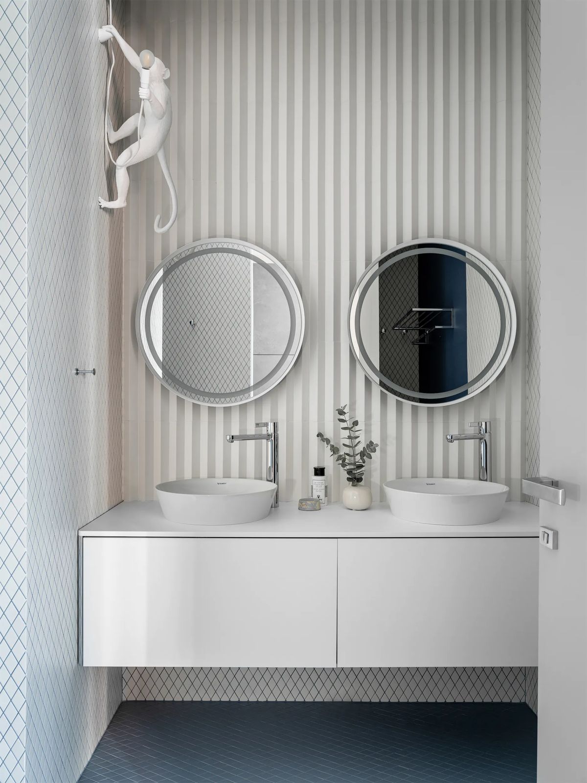Bathroom with two vessel basins on a white floating vanity, round lit mirrors and a white monkey lamp