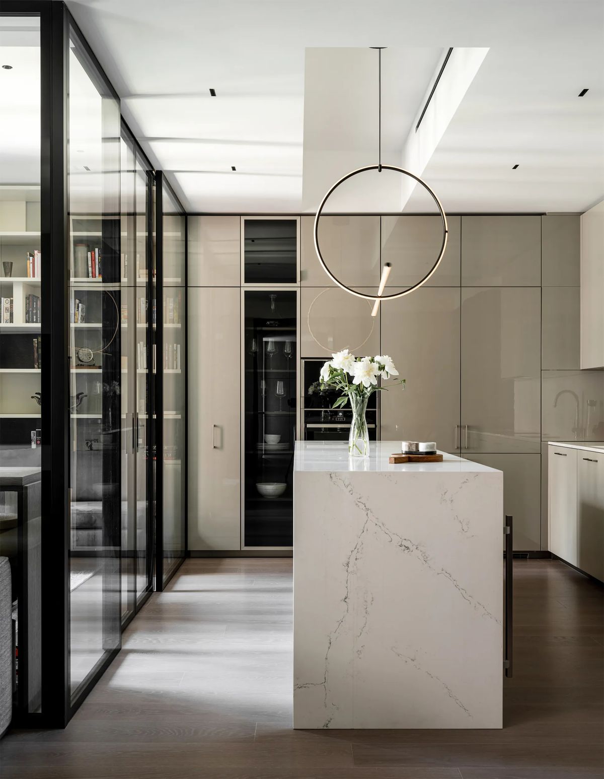 Kitchen with a veined white stone island, ring pendant light and glass-fronted library partition