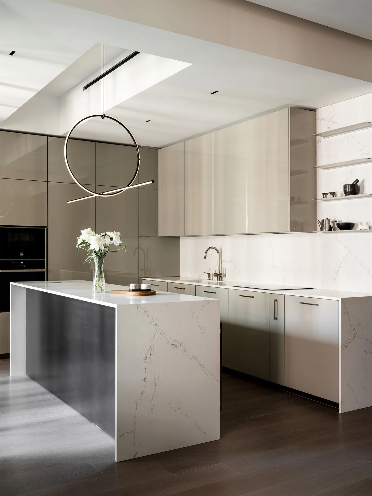 Open kitchen with a waterfall stone island, glossy taupe cabinets, open shelves and a hoop pendant