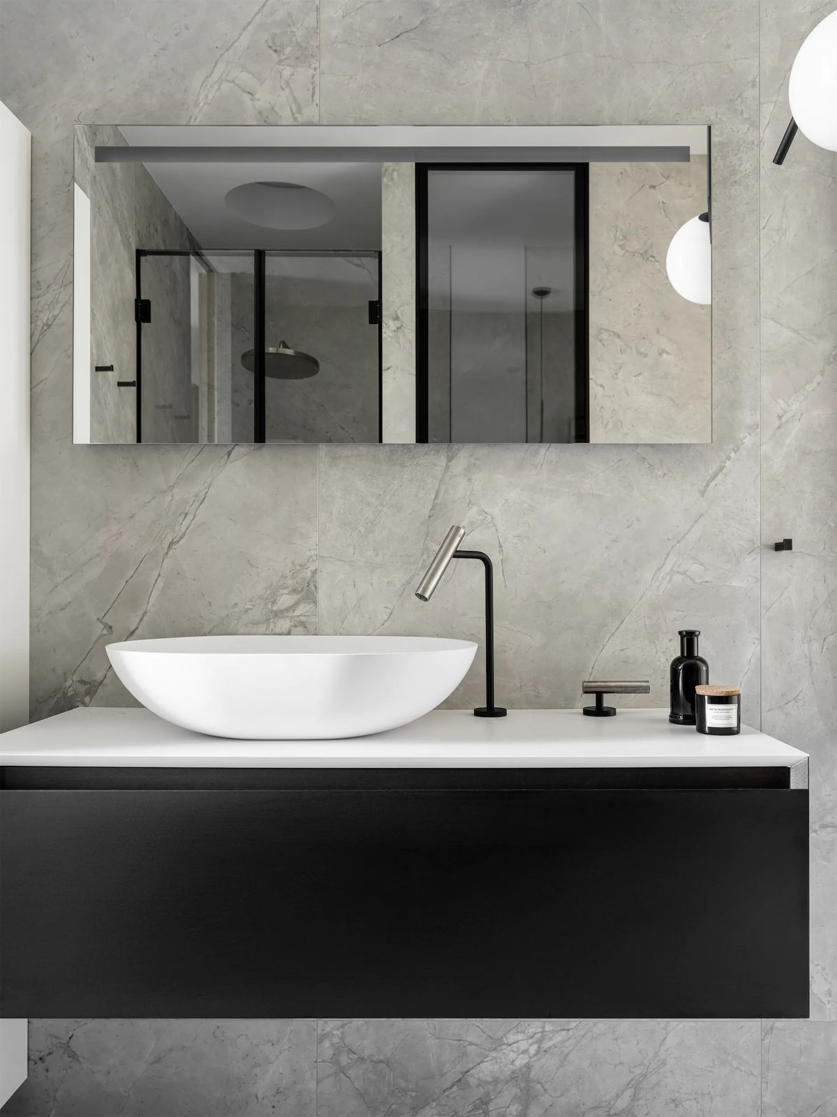 White oval vessel basin on a black floating vanity against grey marble, with a black tap and mirror
