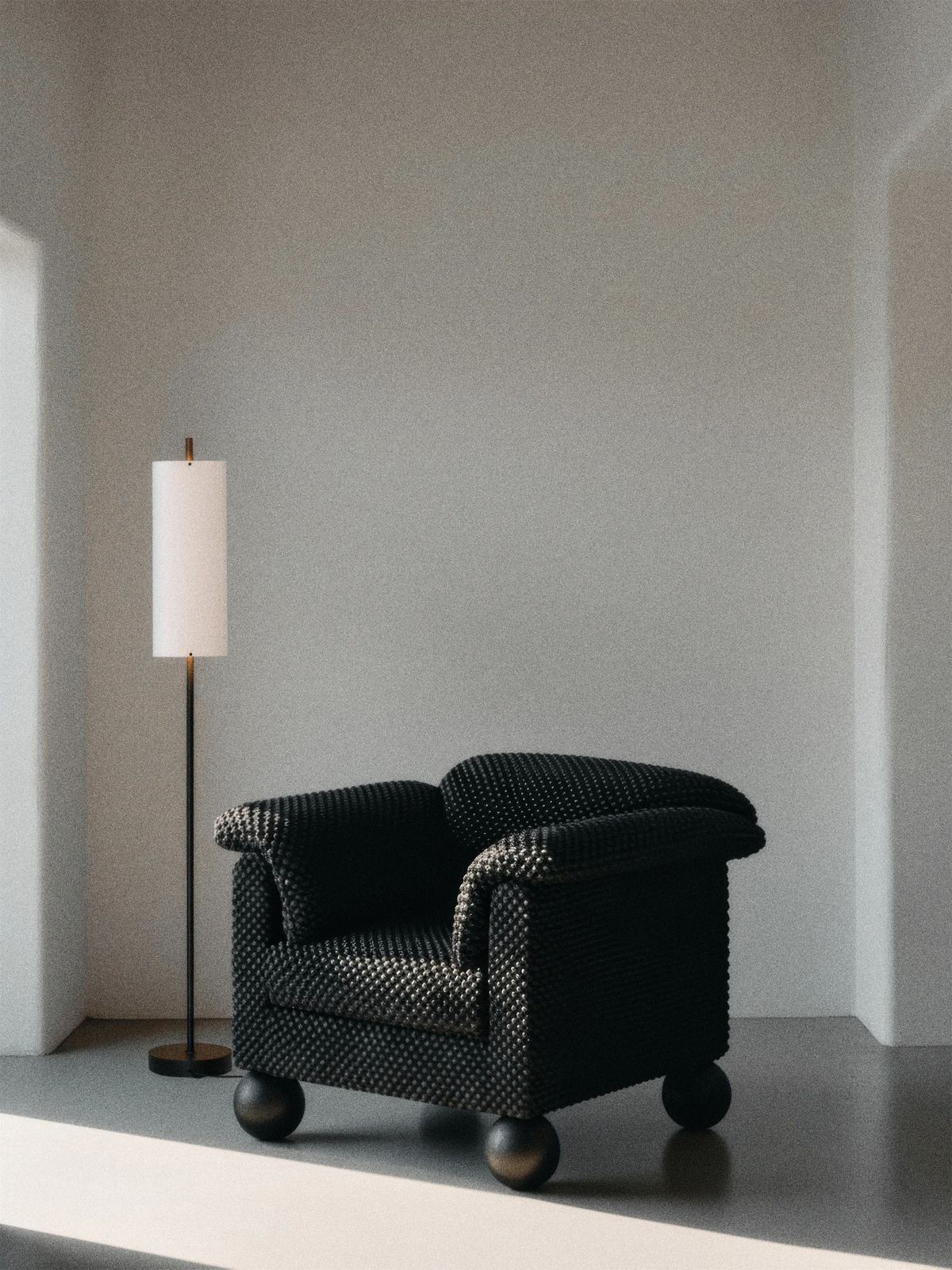 Black beaded-texture armchair on dark ball feet beside a slim floor lamp in a pale grey room