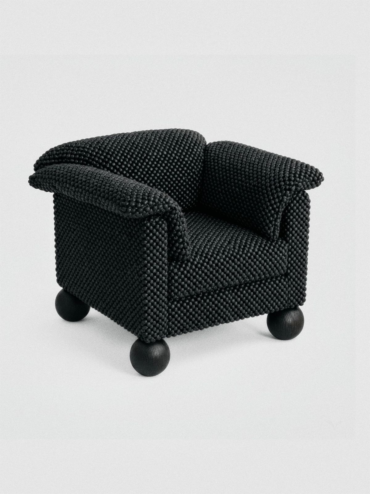 Rodnenkiy armchair in black nubbly upholstery with rolled arms and black ball feet on white
