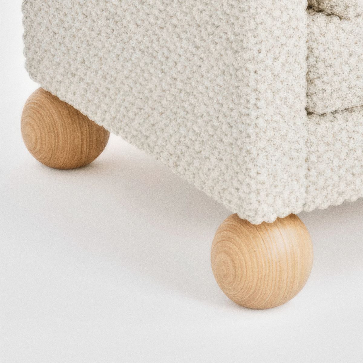 Close-up of the cream textured upholstery meeting two turned natural wood ball feet