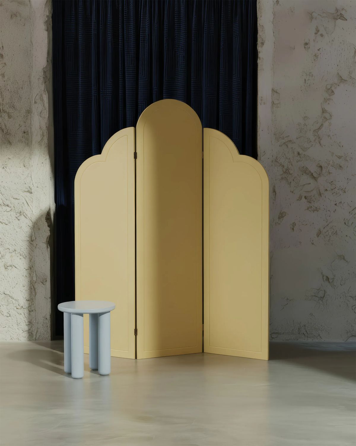 Pale yellow screen with arched panels beside a small light blue stool against a textured plaster wall