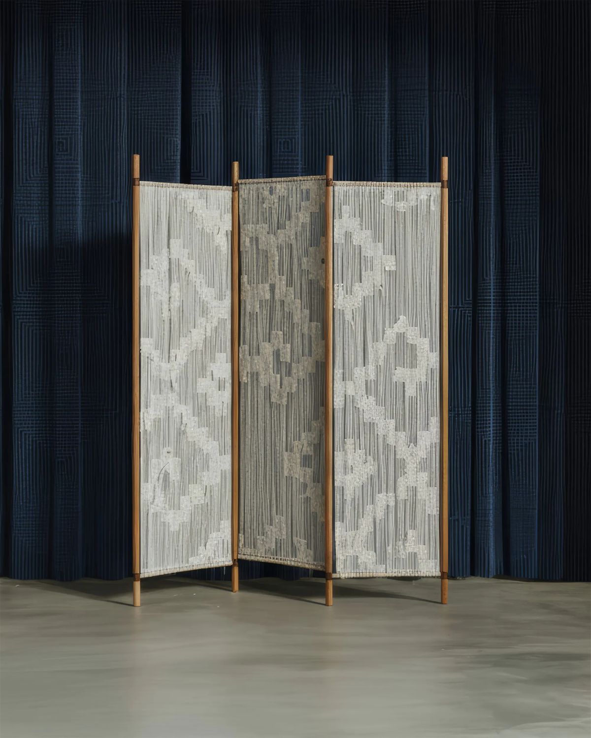 Folding screen of white woven cord with a geometric pattern strung between slim wooden poles