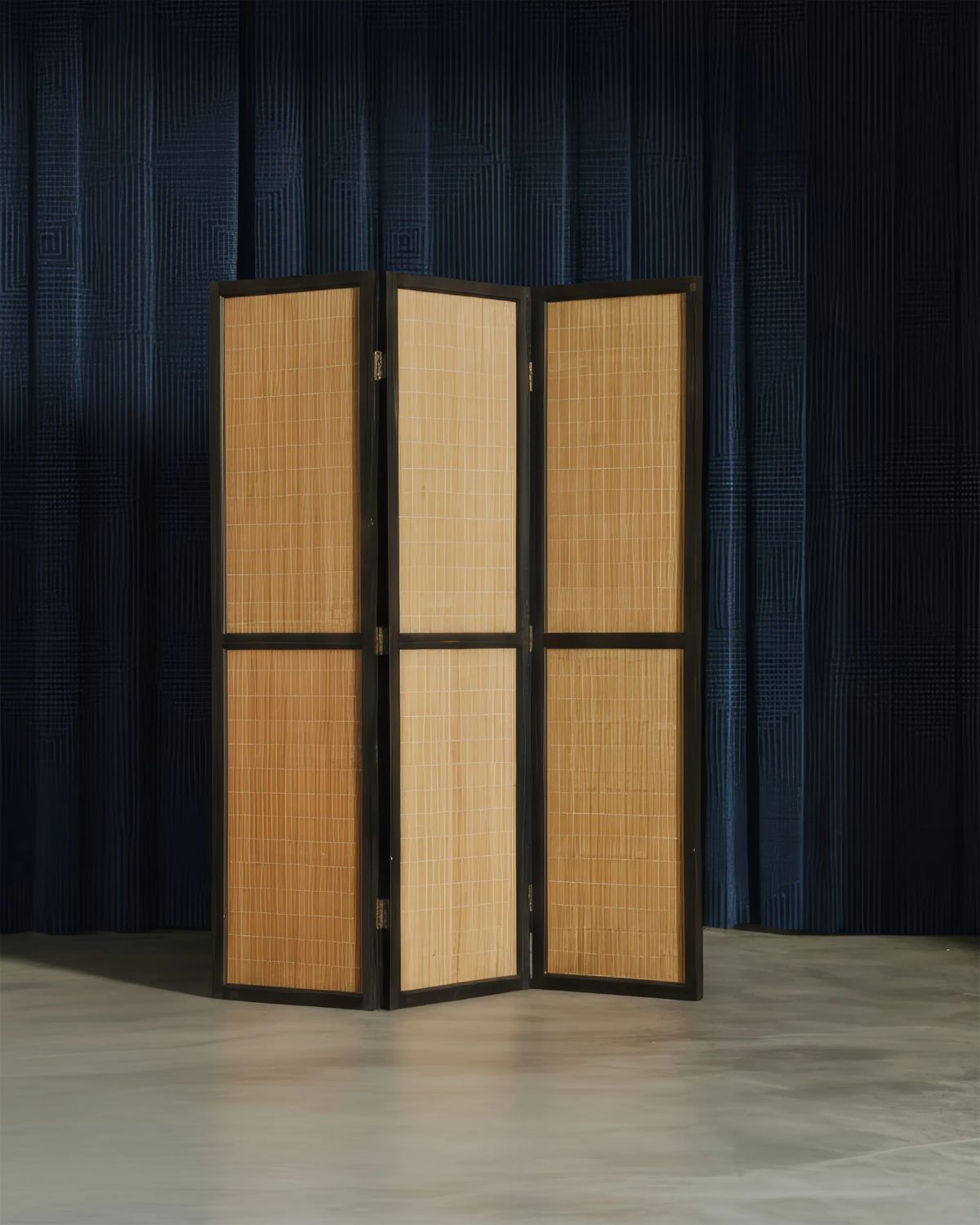 Three-panel screen of honey-coloured woven cane set in a black frame against a navy curtain