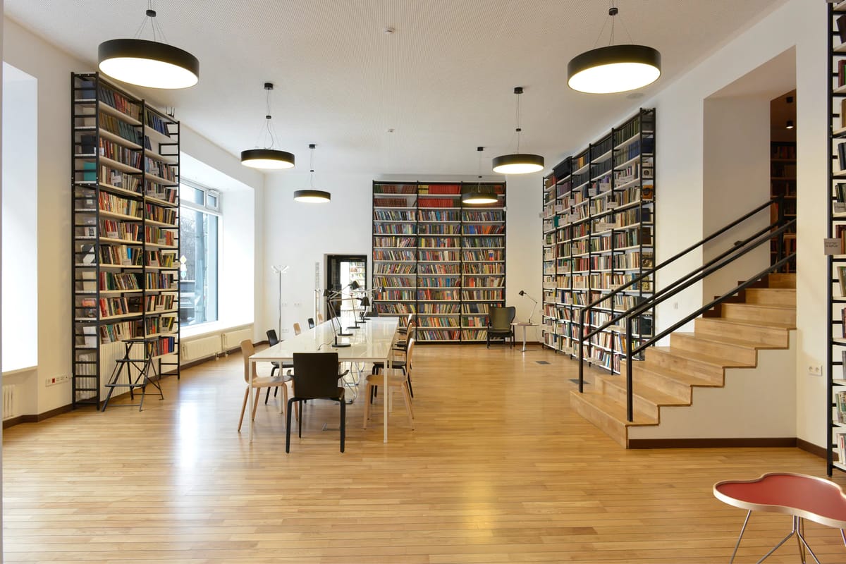 Library hall with tall black steel bookshelves, oak floor, round pendants and a wooden staircase