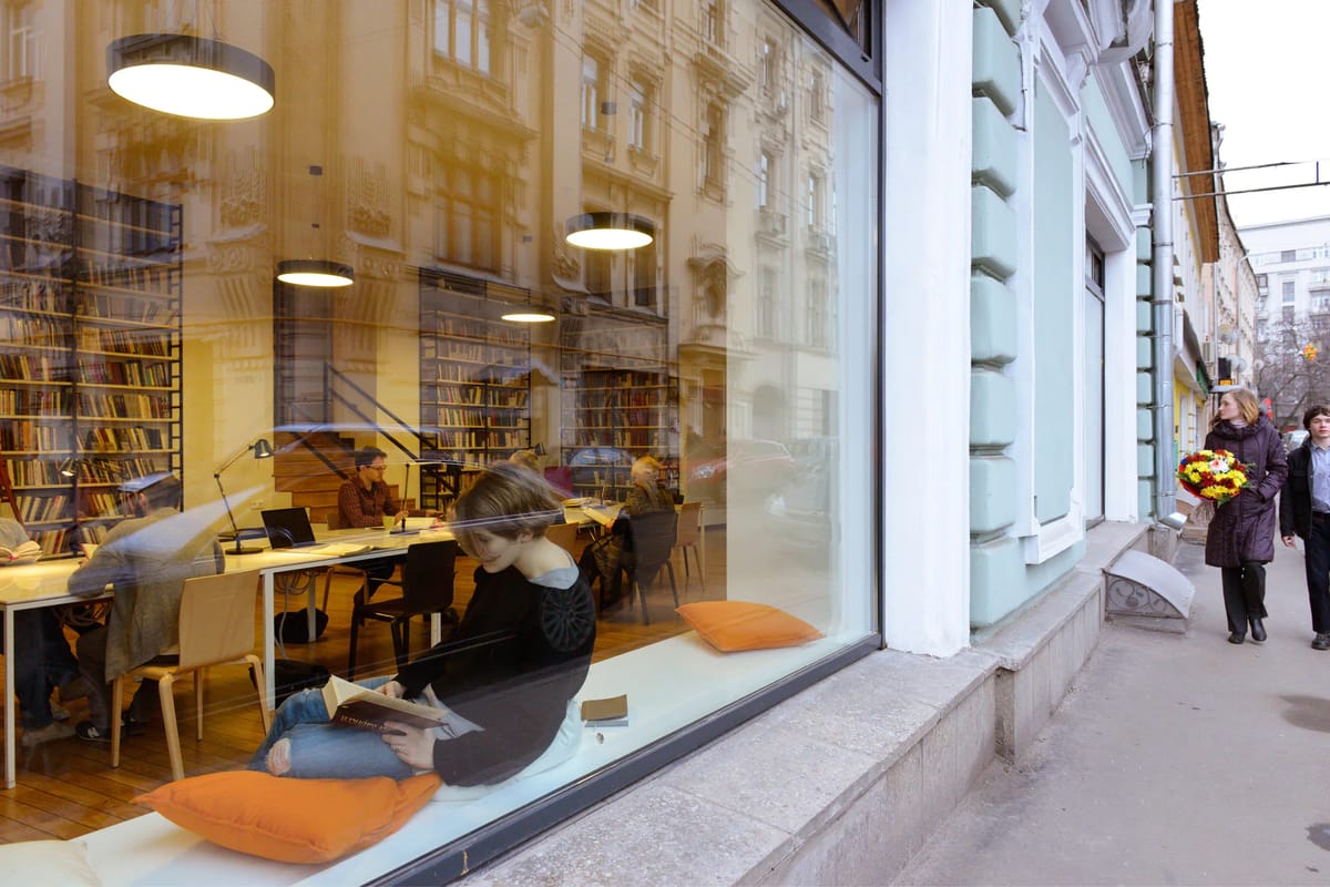 Street window of the Dostoevsky library with a reader on orange cushions and passers-by on the pavement