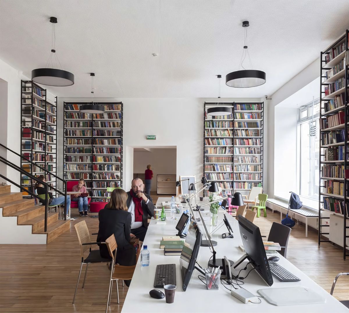 Readers at a long white table with lamps and computers among floor-to-ceiling black steel bookshelves
