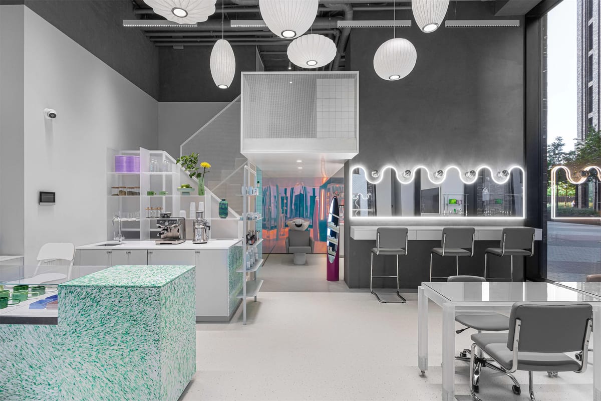 Open salon floor with paper pendant lamps, wavy illuminated mirror bar and grey chairs by the street window