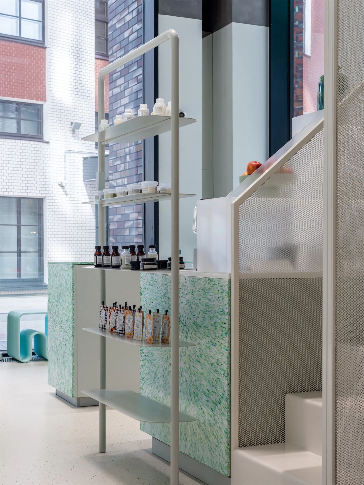 Slim pale steel rack of hair products beside a green speckled counter and perforated metal stair