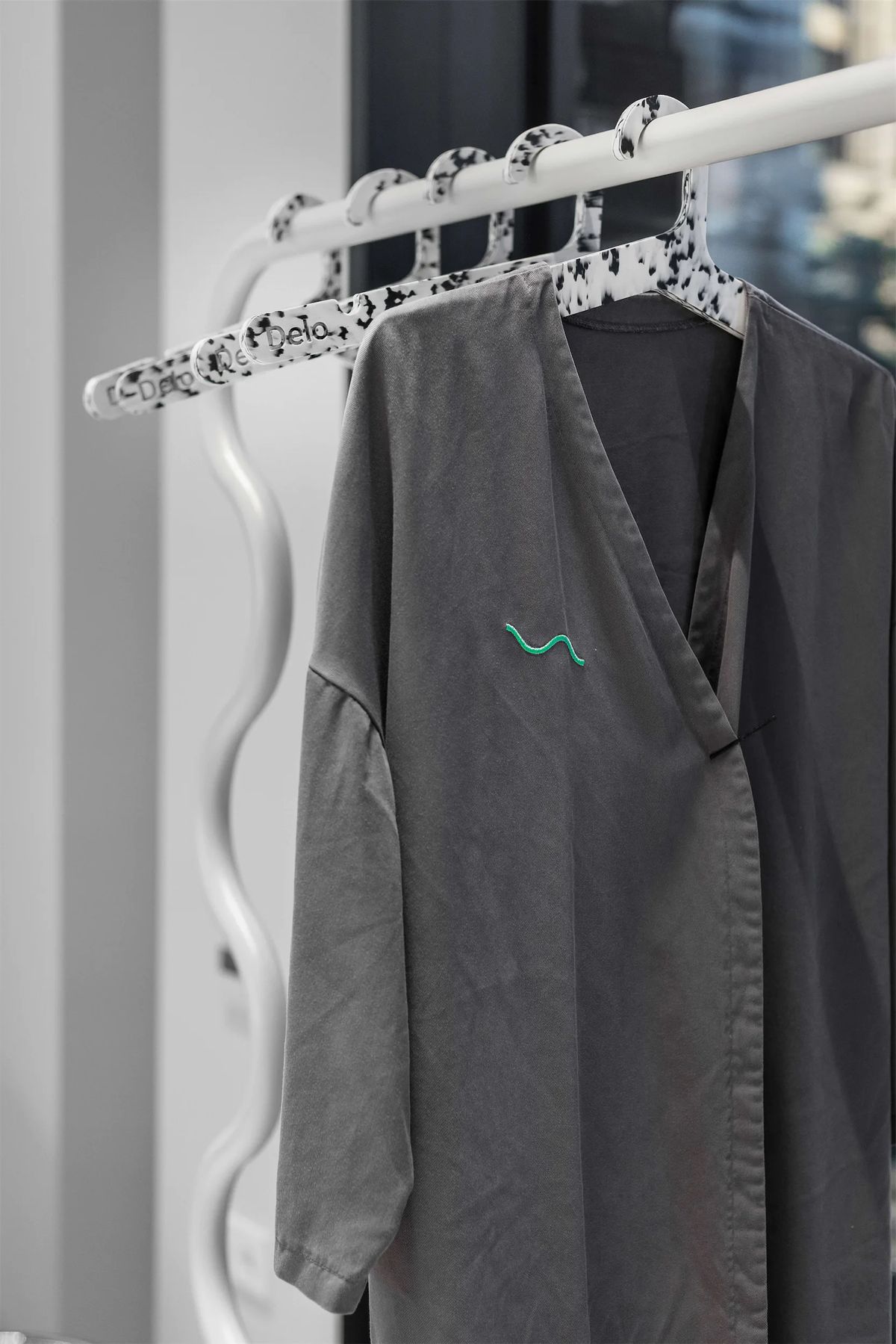 Grey salon robe embroidered with a green squiggle on speckled hangers and a wavy white rail