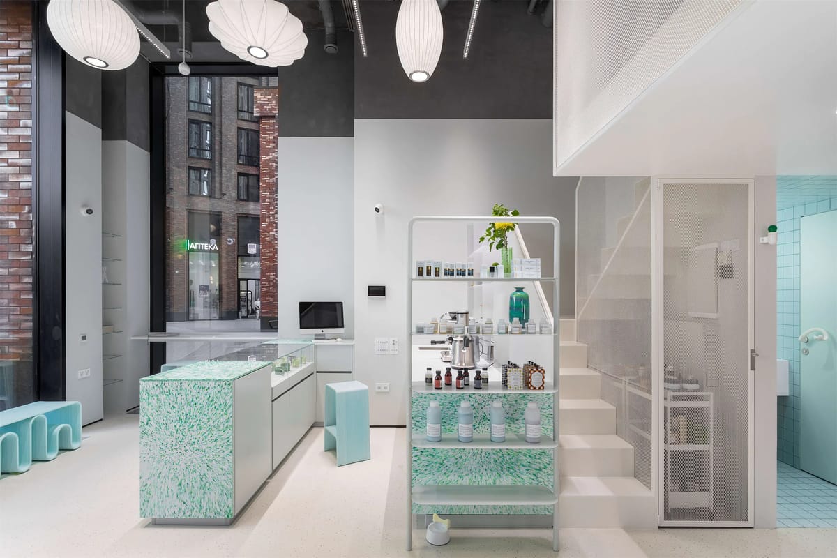Reception with green speckled counter, product rack and white stair up to a mesh-clad mezzanine