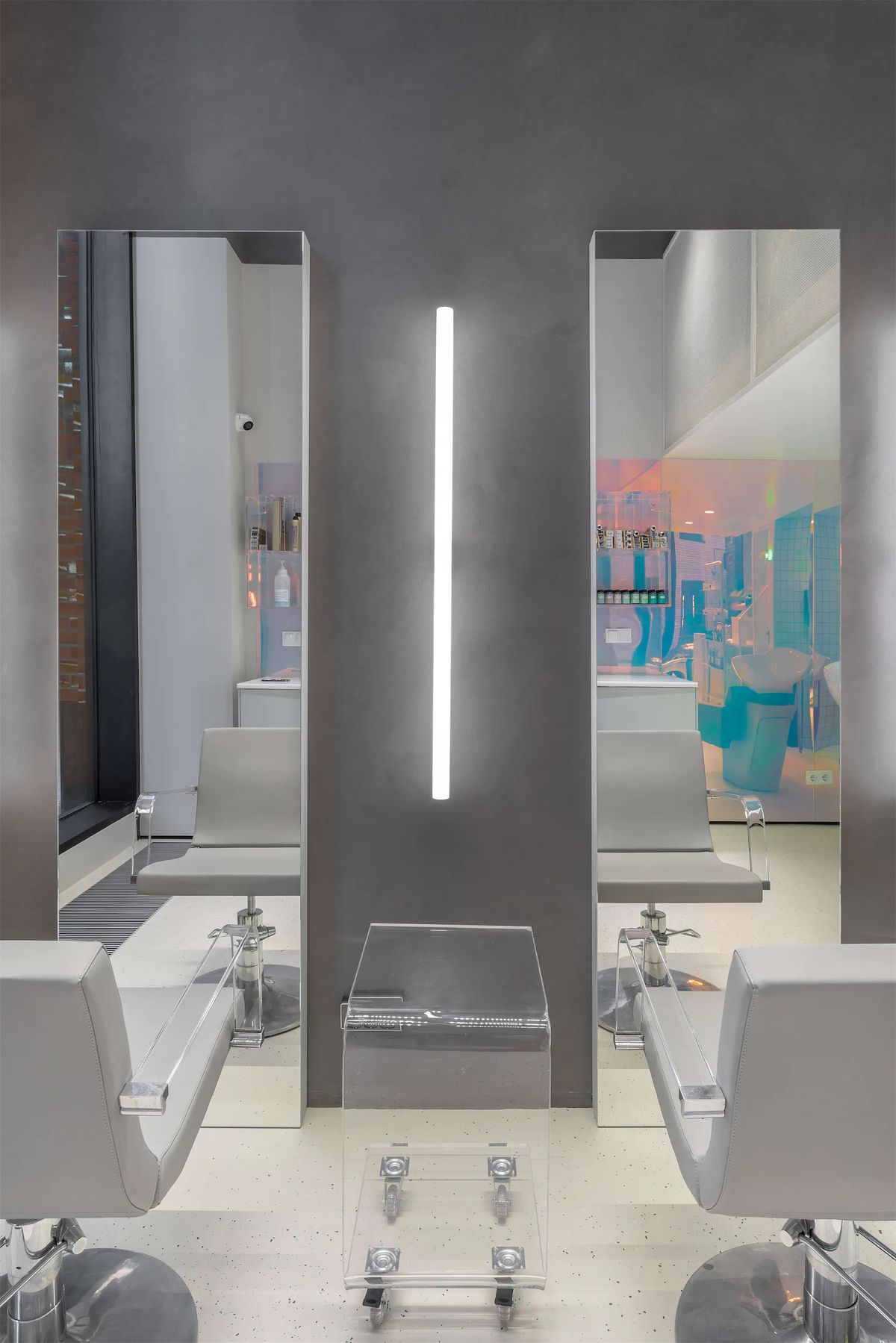 Two styling stations with tall mirrors, grey salon chairs and a clear acrylic trolley against a grey wall