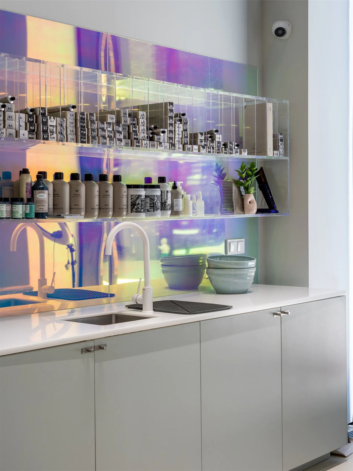 Colouring station with acrylic shelves of hair dye boxes in front of an iridescent dichroic backsplash