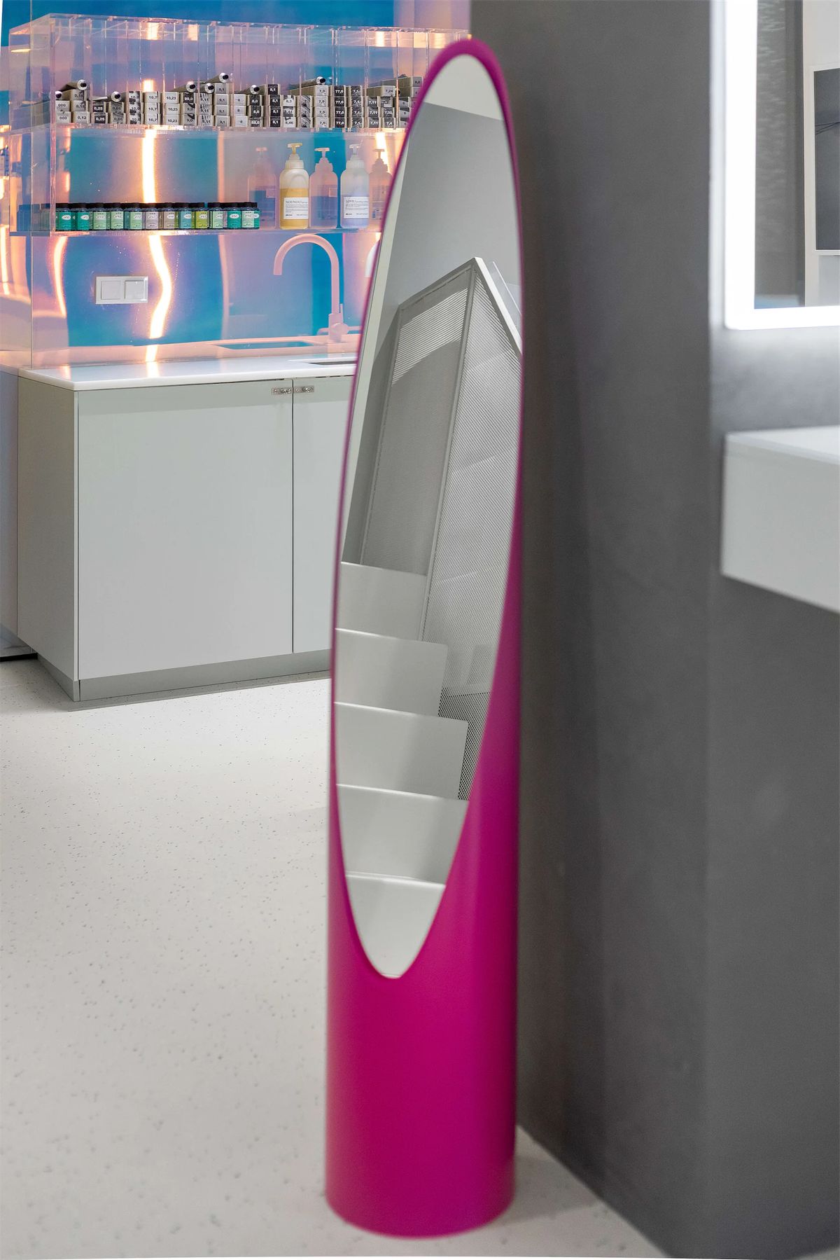 Magenta freestanding oval mirror reflecting the white stair, with the iridescent colour bar behind