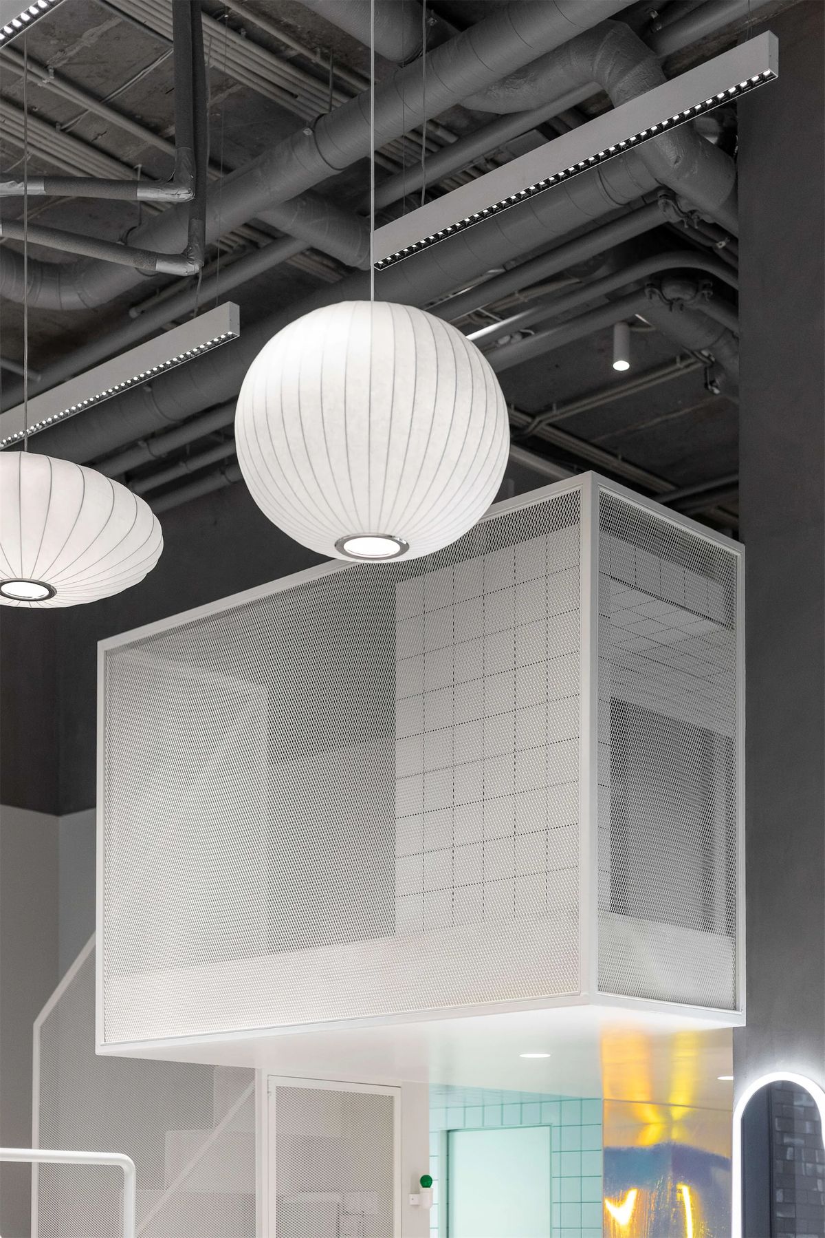 Perforated white metal mezzanine box under exposed ducts and round paper pendant lamps
